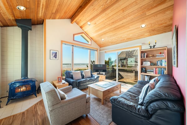 Settle into this cozy living room with vaulted wood ceilings, a wood-burning stove, and stunning coastal views through large windows. Perfect for unwinding after a day exploring the area.