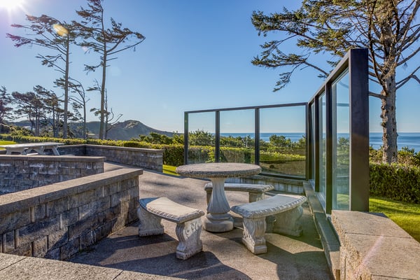 Modern coastal property features stone terracing and panoramic ocean views with mountain backdrop.