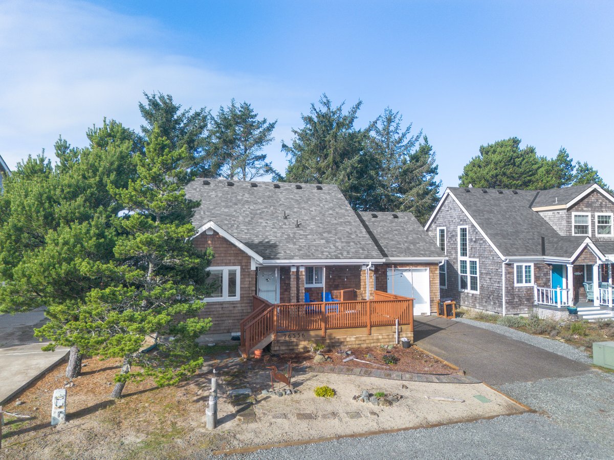 Charming coastal retreat with weathered shingle siding and expansive wooden deck nestled among mature trees in peaceful neighborhood.