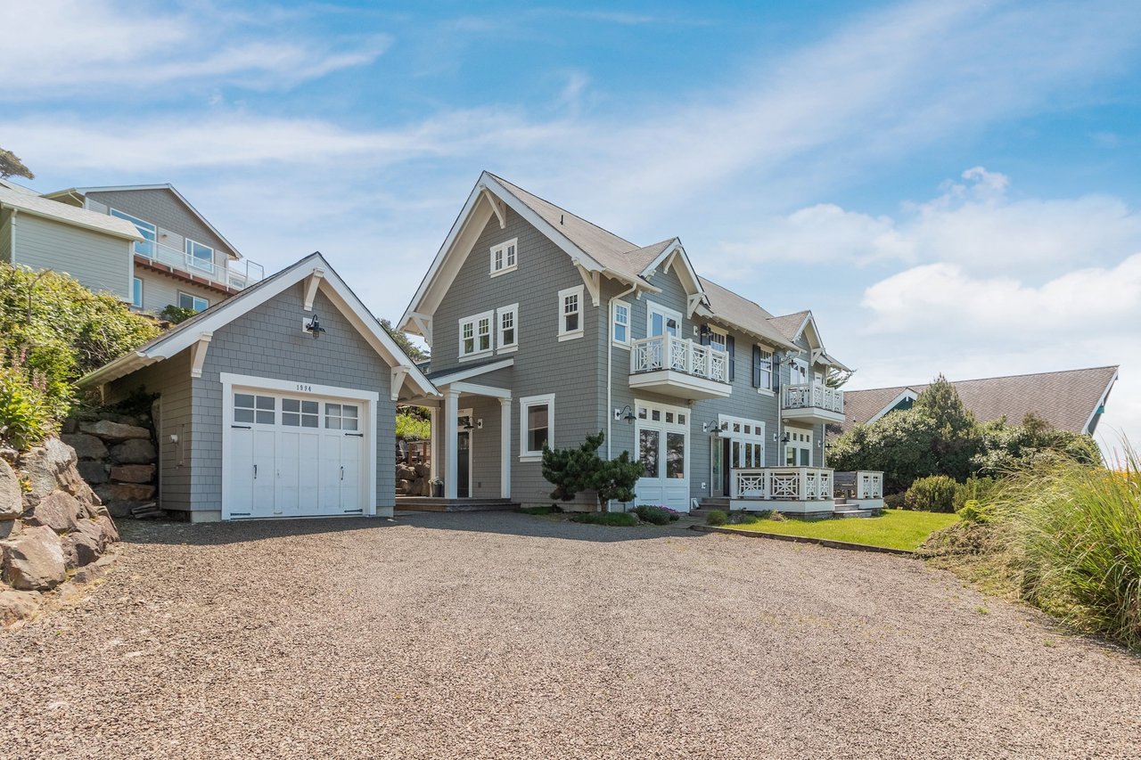 Charming coastal-style home with classic shingle siding, featuring a spacious driveway and well-maintained landscaping, located in a tranquil neighborhood setting.