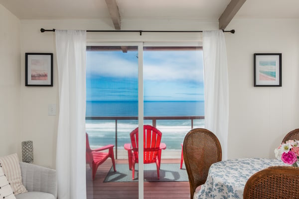 Step through glass doors onto your private deck where vibrant red chairs frame an endless ocean horizon—your morning coffee spot with the sound of waves.