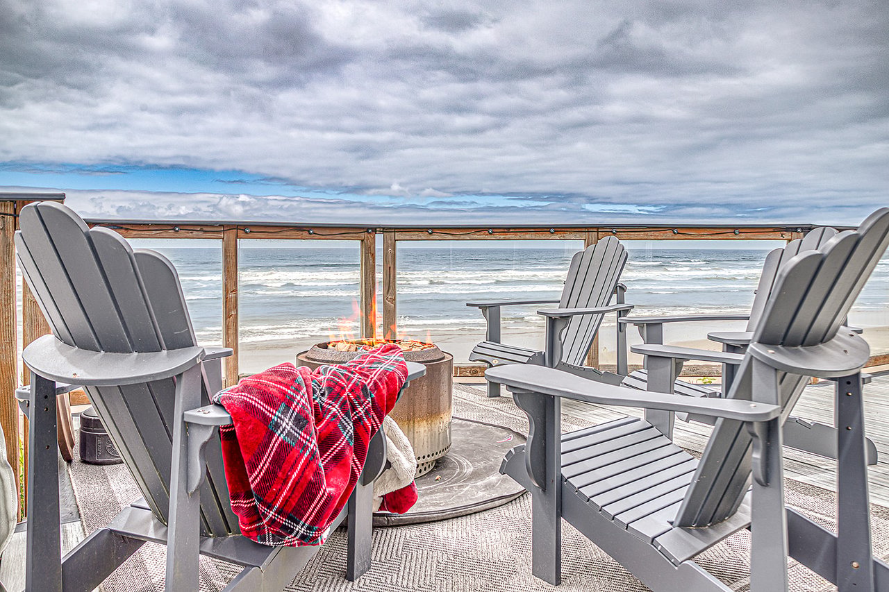 Private beachfront deck with Adirondack chairs and fire pit, where gentle ocean breezes meet panoramic views of rolling waves and sandy shores.