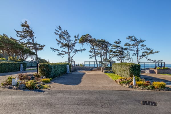 Coastal property entrance features manicured landscaping and mature trees, creating an elegant arrival experience near the ocean.