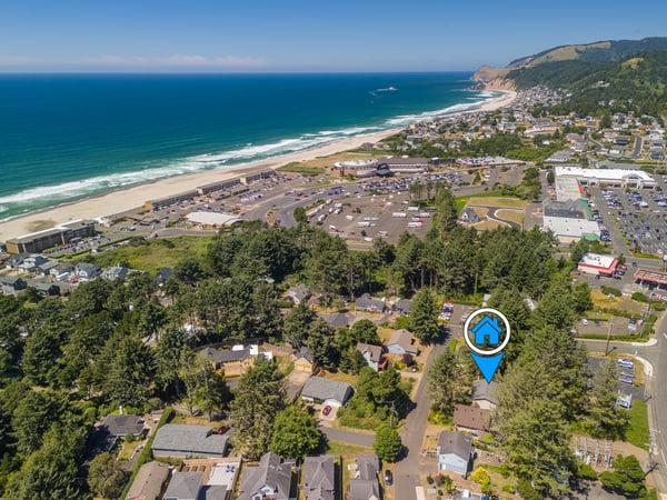 The property sits in a charming coastal neighborhood with the ocean and sandy beach just moments away, surrounded by lush green hills and sweeping seaside views.