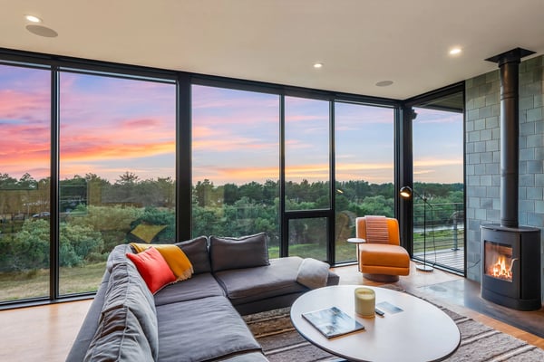 Unwind in this stylish living room with panoramic windows framing breathtaking sunsets and natural views—your cozy retreat with a crackling fireplace and modern comfort.