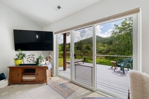 Step into your bright living room where sliding glass doors frame stunning mountain and lake views. Relax with your favorite show or step outside to enjoy your private deck overlooking peaceful natural scenery.