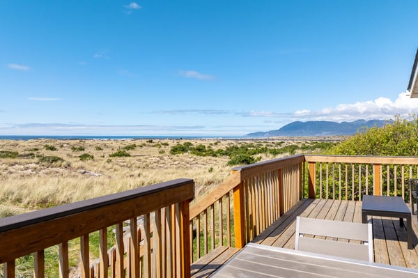 Stunning mountain and coastal views stretch across rolling grasslands from this elevated wooden deck with comfortable seating.