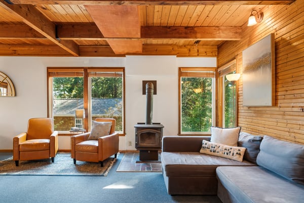 Curl up by the wood-burning fireplace in this inviting living room, where vaulted wood ceilings and garden views through large windows create your perfect retreat.