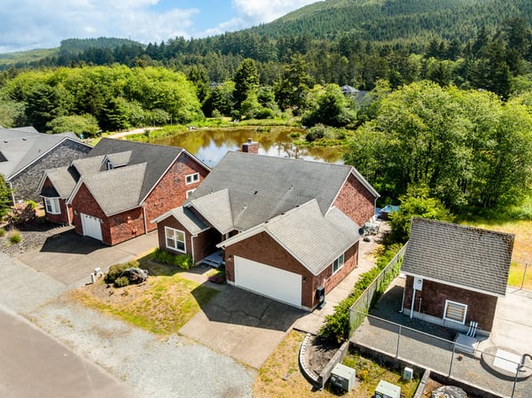 Aerial view of residential properties nestled beside a tranquil pond, surrounded by lush forests and mountains, showcasing the peaceful natural setting of the vacation rental area.
