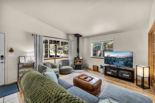 Unwind in your cozy living room with soft seating, a wood-burning stove, and sunlight streaming through large windows. Your mountain escape awaits.