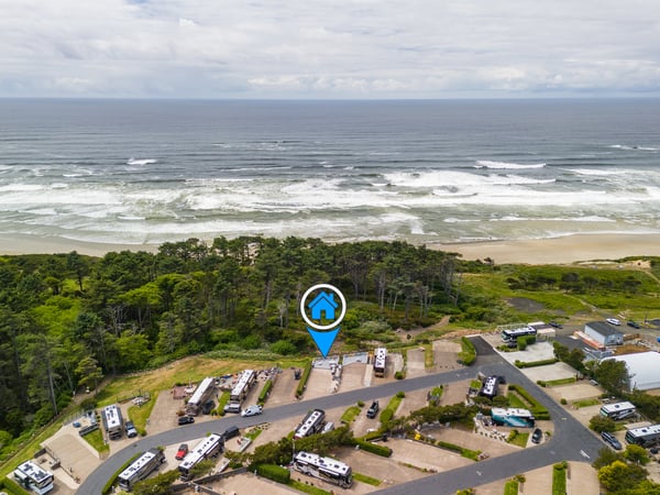 Aerial view of the coastal property situated between lush forestland and sandy beach with rolling ocean waves in the background.