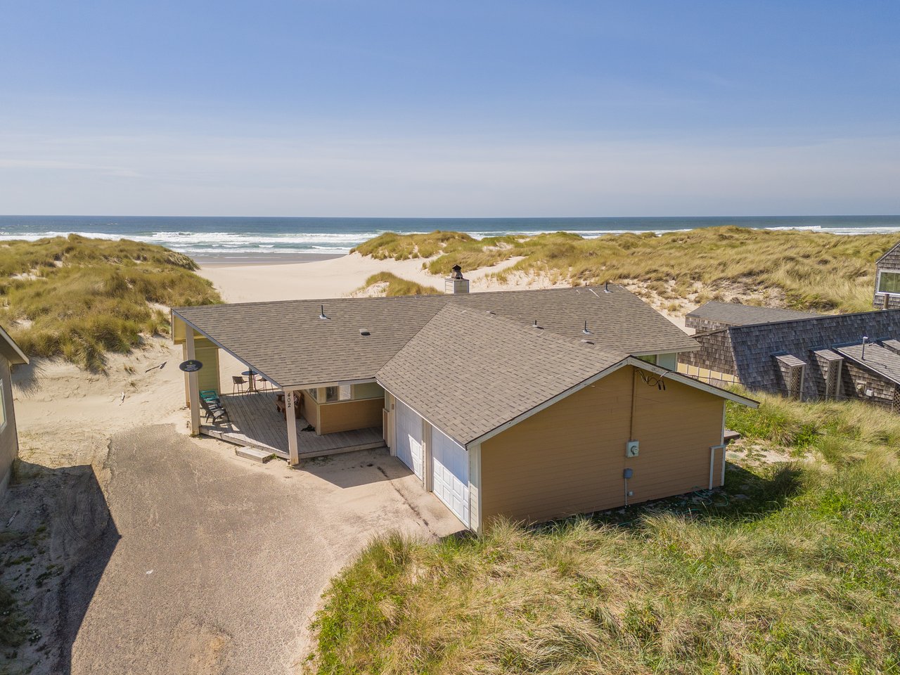 A secluded beachfront property nestled among coastal dunes, offering direct access to pristine sands and ocean surf under clear blue skies.