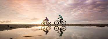 Two people riding fat tire bikes on the beach at sunset